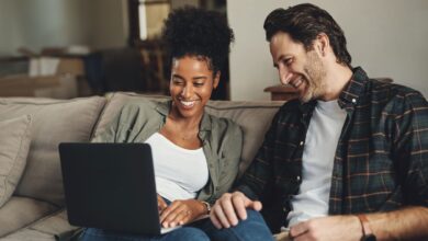 A couple on the couch smiling at a laptop on the woman's lap