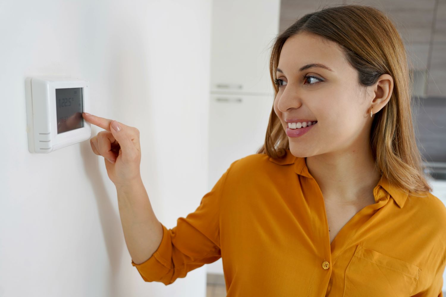 Woman wearing an orange blouse adjusting a thermostat