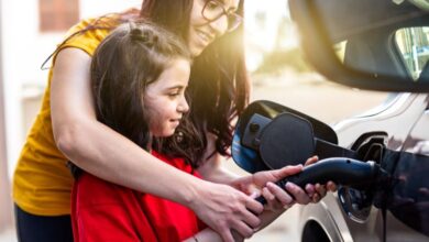 Woman and child plugging in an electric vehicle for charging.
