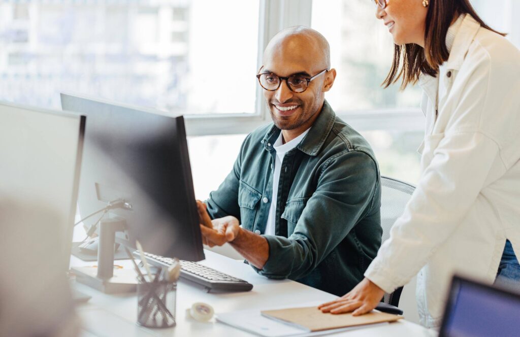 Man working on computer with coworker standing next to him