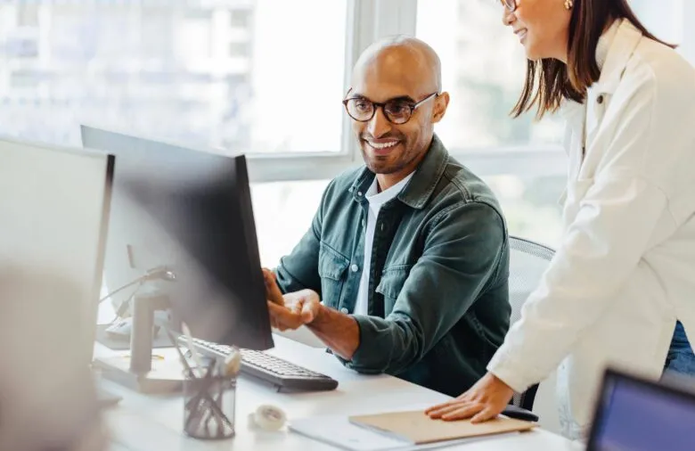 Man working on computer with coworker standing next to him